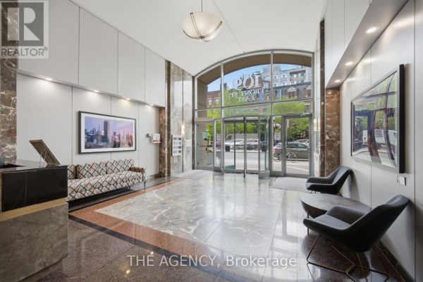 Building lobby with marble floors, patterned sofa, modern chairs, and artwork near large glass entrance. - 643 - 109 Front Street E, Toronto