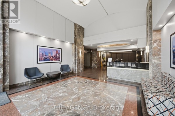 View of the lobby with patterned sofa, two chairs, coffee table, and reception desk area. - 643 - 109 Front Street E, Toronto