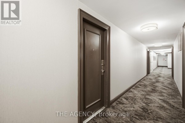 Hallway in apartment building with textured walls, brown doors, patterned carpet, and modern light fixtures. - 643 - 109 Front Street E, Toronto