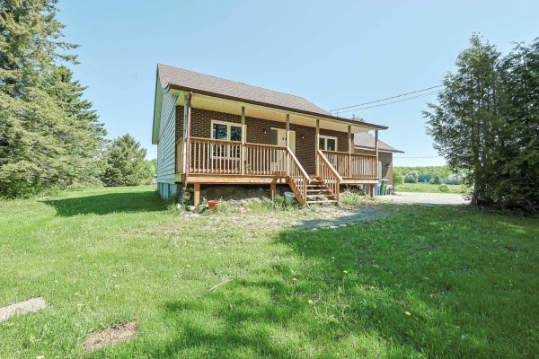 Exterior view of a house with a wooden porch, brick and vinyl siding, and a grassy yard. - 643 Ch. Pierre-laporte, L Ange Gardien