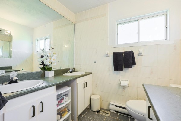 A bathroom with a double vanity, green countertops, white tiled walls, and a toilet. - 643 Ch. Pierre-laporte, L Ange Gardien