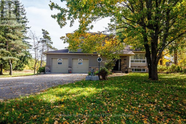Driveway leading to a house with a stone facade and a three-car garage. - 64312 Dufferin County Road 3, East Garafraxa