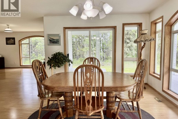 Oak dining table with six chairs in a room with large windows and wood floors. - 6436 Erickson Road, 100 Mile House