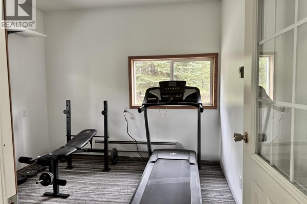 Home gym room with a treadmill, weight bench, and a window facing the woods. - 6436 Erickson Road, 100 Mile House