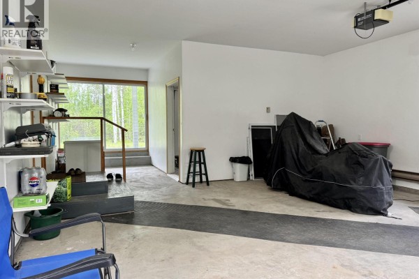 Interior of a spacious garage with concrete floor, a covered motorcycle, and shelving. - 6436 Erickson Road, 100 Mile House