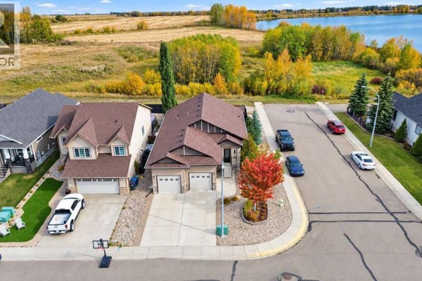 Aerial view of a suburban street with houses, cars, and a distant lake surrounded by autumn trees. - 6444 Cedar Way, Innisfail