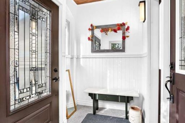 Interior entryway with white paneled walls, a dark bench, a decorative mirror, and a stained-glass front door. - 6444 Cedar Way, Innisfail