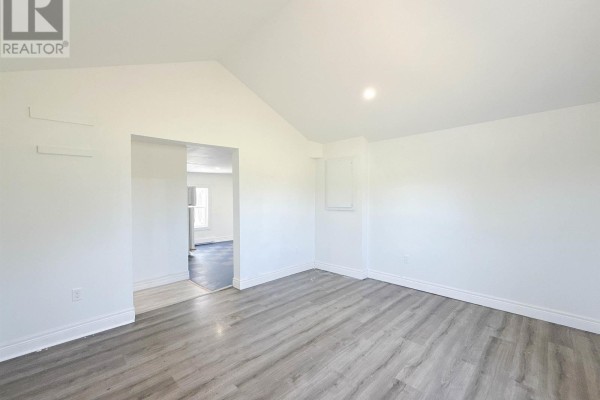 Living room with white walls, vaulted ceiling, and grey wood-look laminate flooring. - 6447 Cardigan Road, Cardigan