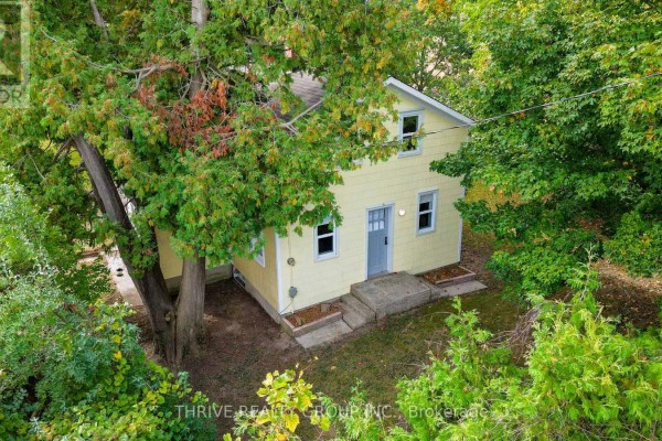 View of a yellow house from the side with a concrete walkway and mature trees. - 648 Concession 13 Concession, Norfolk