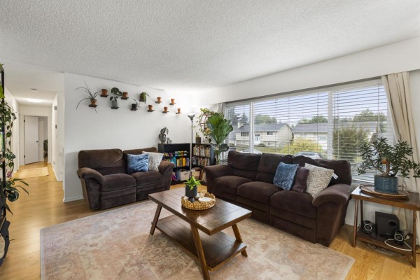 Living room with two brown sofas, a coffee table, and large window overlooking the street. - 6486 Fern Street, Sardis South, Chilliwack