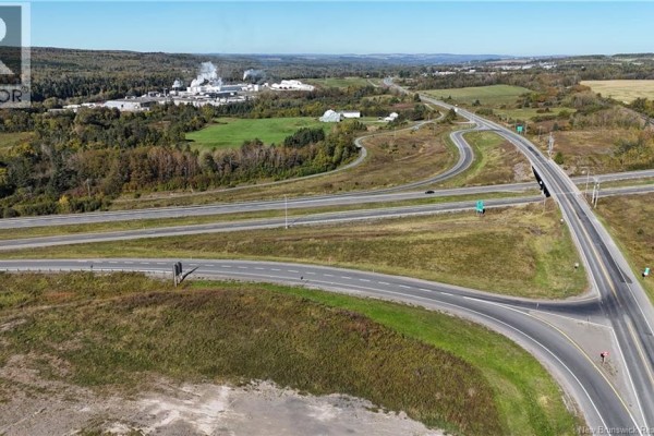 Aerial view of a highway interchange with surrounding fields, trees, and industrial buildings in the distance. - 649 Madawaska Road, Grand Sault/grand Falls