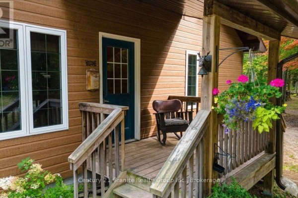 Close-up of the covered front porch with a rocking chair, flower baskets, and a doorbell. - 649 Madawaska Road, Hastings Highlands