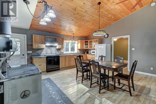 Kitchen and dining area with light wood cabinets, wood plank ceiling, wood floor, and dining table. - 649 Madawaska Road, Hastings Highlands