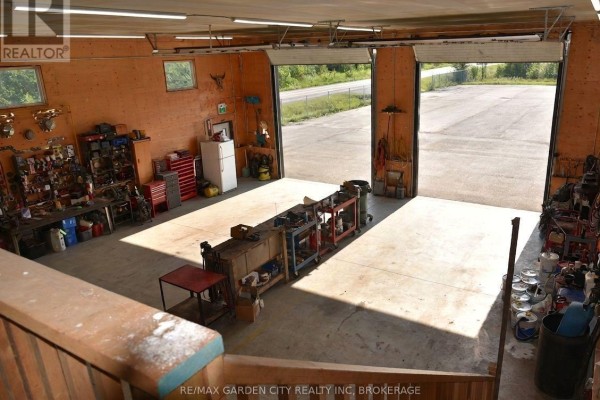 Interior view of a workshop with tools and equipment, featuring two large open garage doors. - 64b Stonebridge Drive, Port Colborne