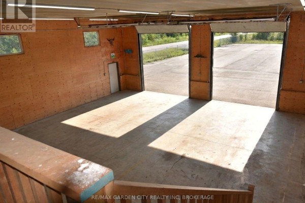 Interior view of a spacious workshop with concrete floors and wood-paneled walls, open garage doors visible. - 64b Stonebridge Drive, Port Colborne