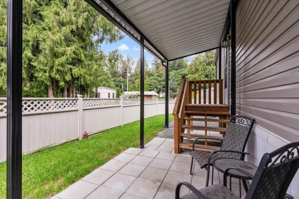 View of a covered patio with two chairs and a small table beside a grey mobile home. - 65 3942 Columbia Valley Road, Cultus Lake East, Cultus Lake