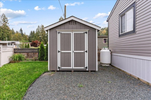 Covered patio with two chairs and a table on a tiled floor, adjacent to a mobile home. - 65 3942 Columbia Valley Road, Cultus Lake East, Cultus Lake