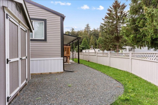 A grey storage shed with double doors stands on a gravel pad next to a mobile home. - 65 3942 Columbia Valley Road, Cultus Lake East, Cultus Lake
