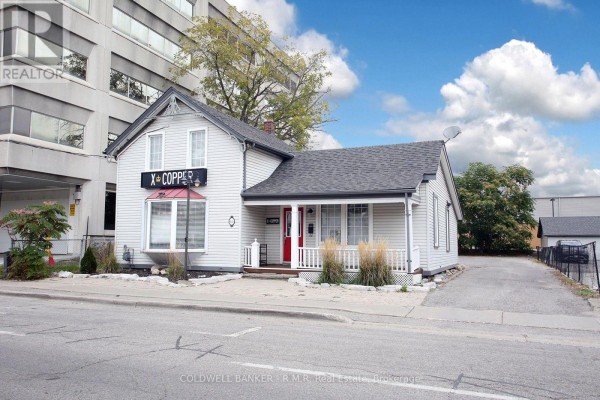 Front view of the light grey commercial building with a grey asphalt driveway on the right. - 65 Albert Street, Oshawa