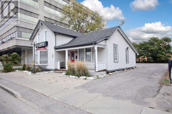 Side view of the light grey commercial building showing a white porch and a driveway. - 65 Albert Street, Oshawa