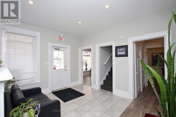Interior hallway with light grey walls, tiled floor, black sofa, and doors leading to rooms. - 65 Albert Street, Oshawa