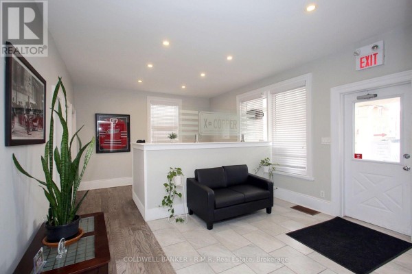 Reception area with light grey walls, tiled floor, black sofa, and glass signage on the counter. - 65 Albert Street, Oshawa