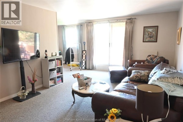 Living room with brown leather sofa, armchair, coffee table, and large sliding glass doors. - 65 Baldoon Road Unit# 11, Chatham