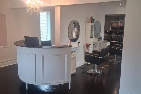 Interior salon view showing a white reception desk and black styling chairs. - 65 Broadway, Orangeville