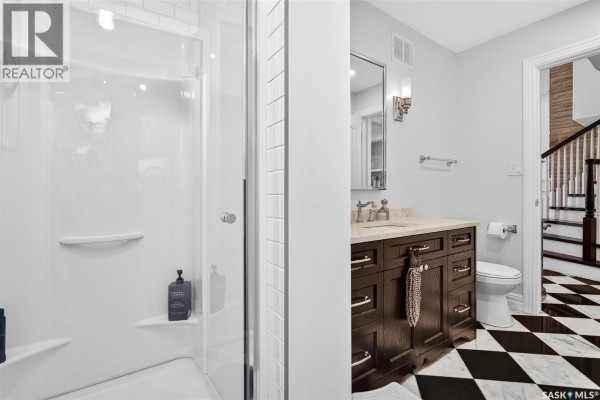 Bathroom with white tiled shower stall, dark wood vanity, and checkerboard marble floor. - 65 Calypso Drive, Moose Jaw