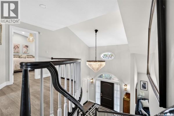 View from the top of a dark wood staircase overlooking the entryway with arched window and chandelier. - 65 Calypso Drive, Moose Jaw