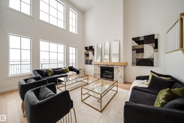 Living room fireplace with stone surround, flanked by artwork and tall windows. - 65 Chartres Cl, St  Albert