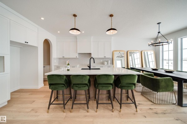Kitchen island with green velvet stools, white cabinetry, and pendant lighting overlooking dining area. - 65 Chartres Cl, St  Albert