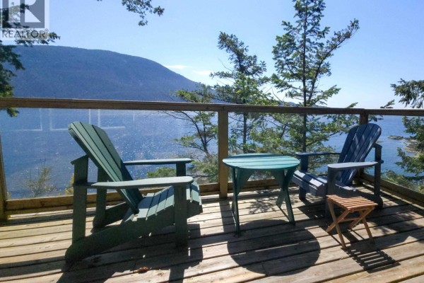 Two Adirondack chairs and a round table on a wooden deck face a panoramic view of water and lush green hills. - 65 Esplanade Road, Keats Island