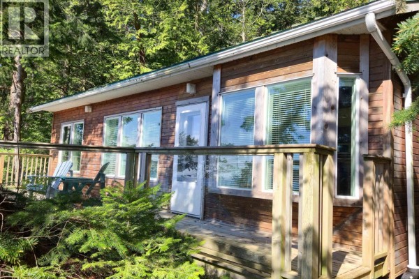 Exterior of a small, wood-sided cabin with multiple windows and a white door, viewed from the deck. - 65 Esplanade Road, Keats Island