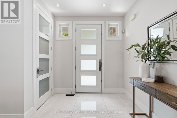Interior entryway with white door, side windows, and a console table with mirror. - 65 Forest Avenue, Mississauga