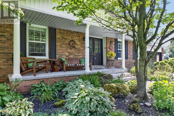 Wooden porch furniture on a covered porch with brick columns and landscaping. - 65 Maplewood Drive, Amaranth