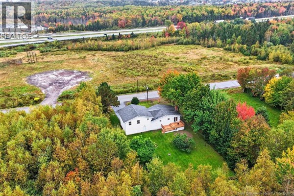 Aerial view of the property from above, showing the house, trees, and nearby highway. - 65 Northwood Road, Moncton