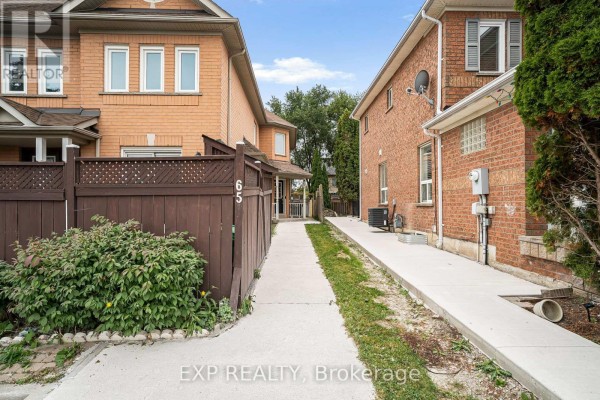 View down paved walkway between brick townhouses with green foliage. - 65 Pressed Brick Drive, Brampton
