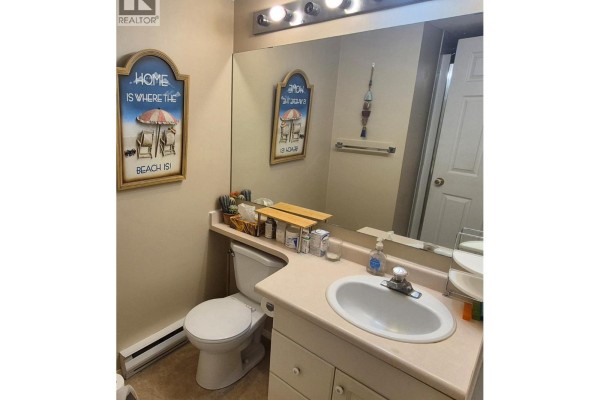 Kitchen with white cabinets, beige countertops, double sink, and stacked washer and dryer. - 650 3 Street Sw Unit# 404, Salmon Arm