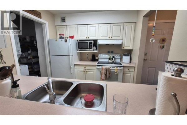Kitchen with white cabinets, beige countertops, white appliances, and a stacked washer and dryer. - 650 3 Street Sw Unit# 404, Salmon Arm