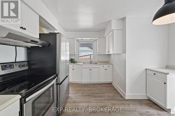 Kitchen with stainless steel appliances, white cabinets, and light wood laminate flooring. - 650 Hillside Drive, Gananoque