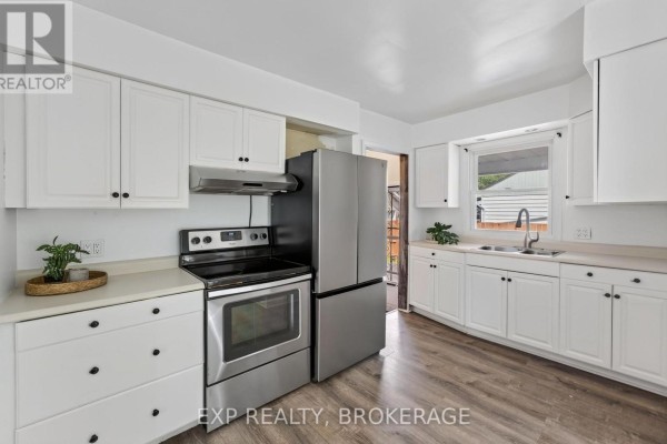 Kitchen with stainless steel range, refrigerator, white cabinets, and laminate flooring. - 650 Hillside Drive, Gananoque