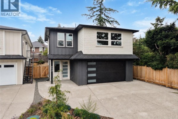 Exterior of a two-story house with a dark grey and white facade, black garage door, and wooden fence. - 650 Wisteria Ridge, Langford