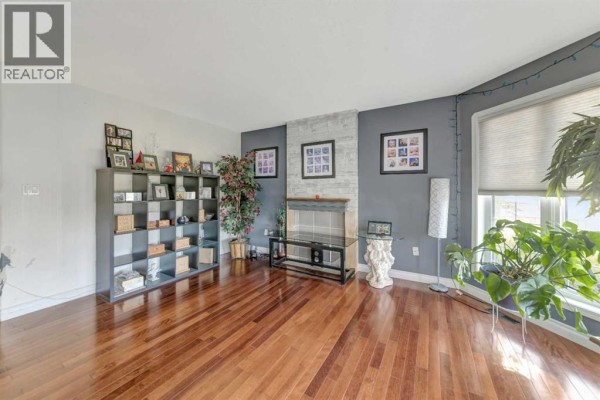 Living room with hardwood floors, a fireplace, large windows, and a gray accent wall. - 6501 39 Street, Lloydminster