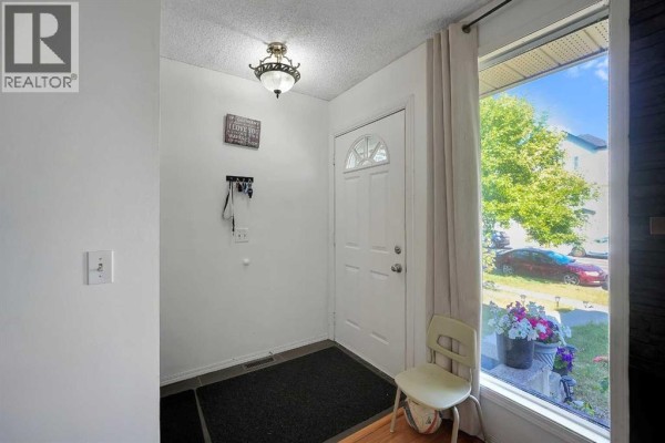 Interior entryway with a white door, dark mat, and a large window overlooking the street. - 6507 Rundlehorn Drive Ne, Calgary