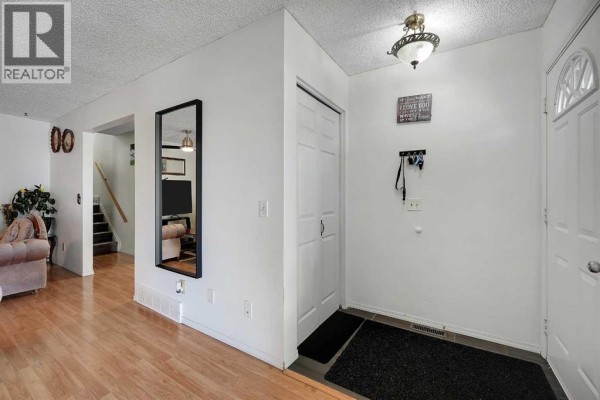 Hallway entrance with white walls, a coat rack, a closet, and a mirror reflecting a staircase. - 6507 Rundlehorn Drive Ne, Calgary