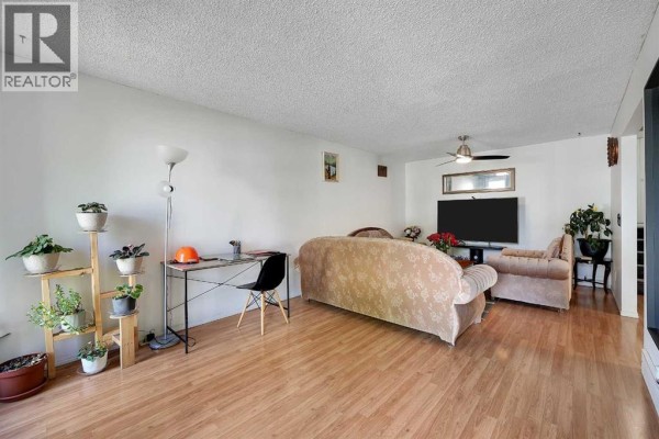 Spacious living area with a couch, chairs, a desk, and a television mounted on the wall. - 6507 Rundlehorn Drive Ne, Calgary