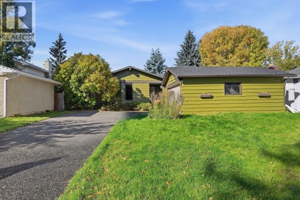 Front view of a green house with a driveway and a separate garage on a sunny day. - 652 Oakwood Place Sw, Calgary