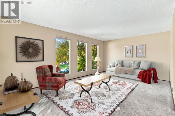 Living room with beige walls, plush carpet, a plaid armchair, sofa, and coffee table. - 652 Oakwood Place Sw, Calgary