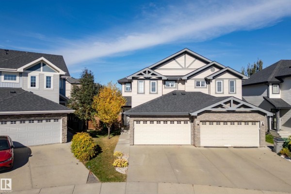 Angled exterior view of a beige duplex with a grey roof and stone accents on the garage doors. - 6520 59 Av, Beaumont